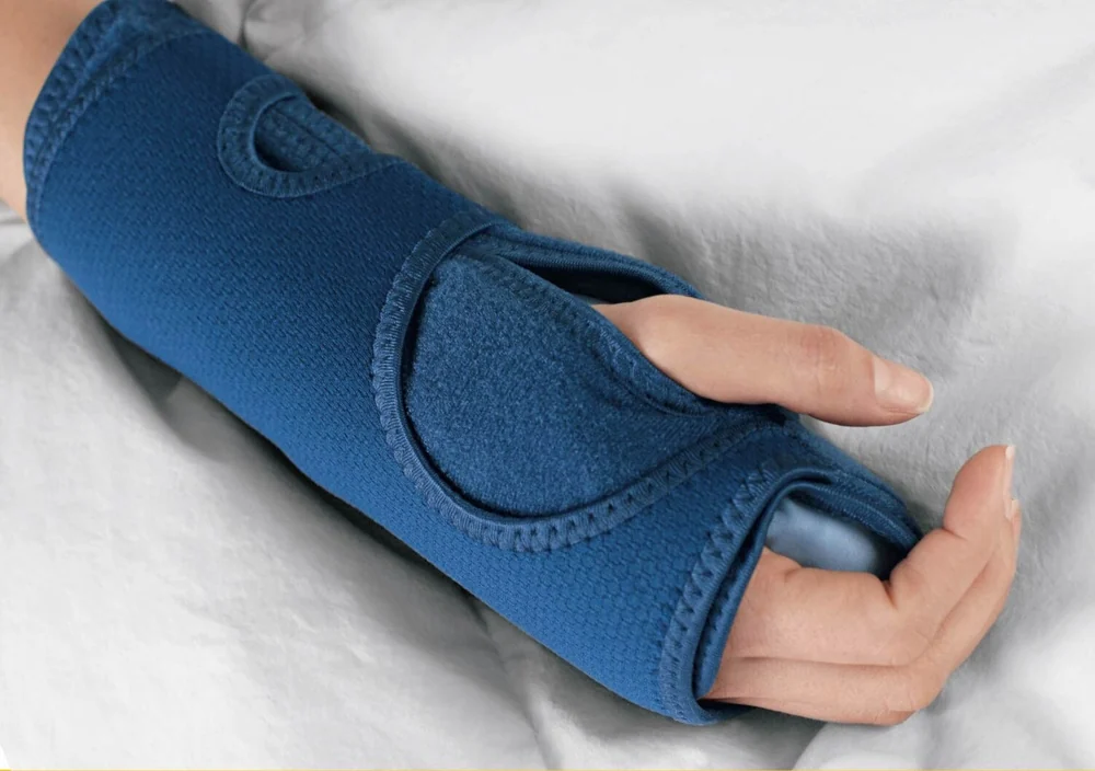 The FUTURO Night Wrist Support, a blue padded night splint, worn on a hand resting on a bed
