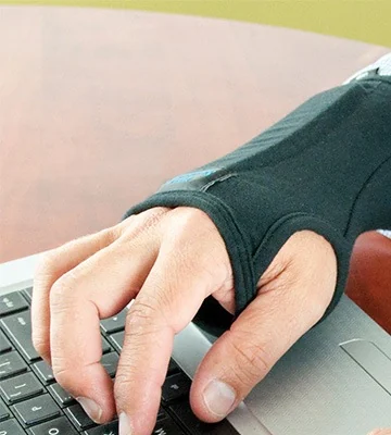 A hand wearing the IMAK RSI SmartGlove while typing on a laptop keyboard